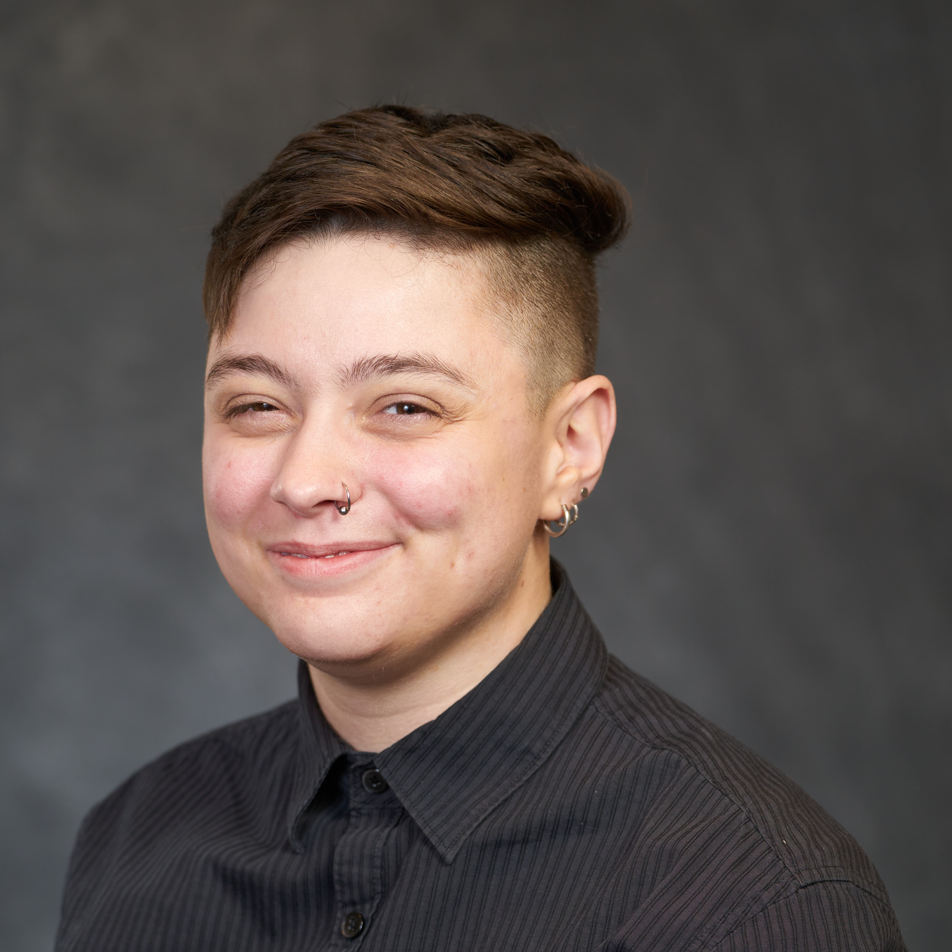 A smiling person with light skin and brown hair looks at the camera